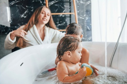 Mother washing her hair while two young children play in a bath